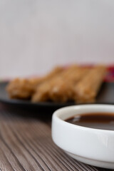 A container of chocolate to accompany churros. In the background, a plate of fuzzy churros.