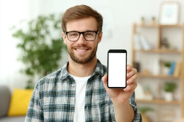 A smiling man in glasses presents a blank screen smartphone in a home setting