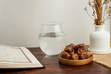 An open Quran beside a bowl of dates and a glass of water on a wooden table, symbolizing iftar during Ramadan. Peaceful Islamic still life concept.