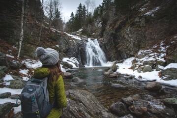 Obraz premium Young female hiker relishing a mountain waterfall amidst early spring snow