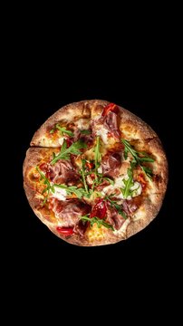 Prosciutto pizza with strachatella cheese, tomatoes and arugula leaves, top view, closeup object. Rotating on black background. Vertical footage
