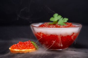 Elegant presentation of red caviar in a glass bowl, garnished with fresh herbs, creates a luxurious culinary experience, perfect for gourmet dining and special occasions.