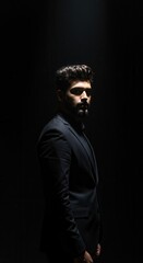 Obraz premium A striking portrait showcases a man in a dark suit, illuminated dramatically from above against a stark black backdrop, creating an atmosphere of mystery and sophistication while highlighting the...