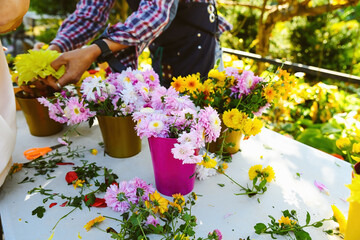 Children and florists creating chrysanthemum bouquets at outdoor workshop, hands arranging flowers...