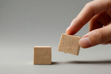 Hand holding a wooden block next to another one on a gray surface, education concept