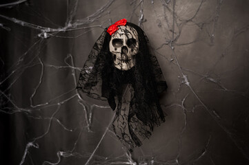 A spooky decorative skull with a black lace veil and a bright red flower against a dark cobweb background. Halloween holiday concept.
