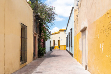 A narrow alleyway with a yellow and blue wall. The alleyway is empty and has a peaceful atmosphere. Historic center of Querétaro, colonial architecture, decorations for the celebration of Mexico's Ind
