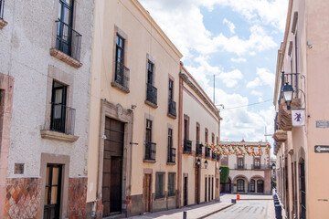 Obraz premium A street with a few buildings and a few people walking around. The street is narrow. Historic center of Querétaro, colonial architecture, decorations for the celebration of Mexico's Independence Day.