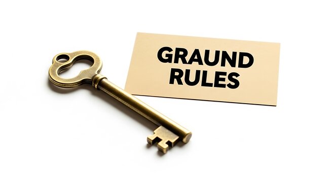 An antique brass key lies next to a card with the words graund rules written on it, isolated on white background