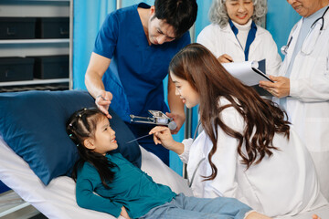 Fototapeta premium Group of Asian doctors and nurses consulting a young child patient in hospital ward. Real people, teamwork, pediatric care, diagnosis, and professional healthcare service.