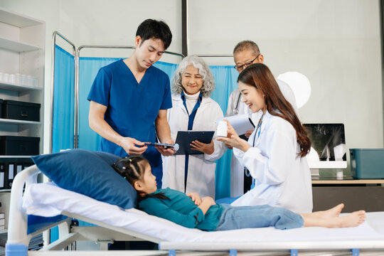 Group of Asian doctors and nurses consulting a young child patient in hospital ward. Real people, teamwork, pediatric care, diagnosis, and professional healthcare service.