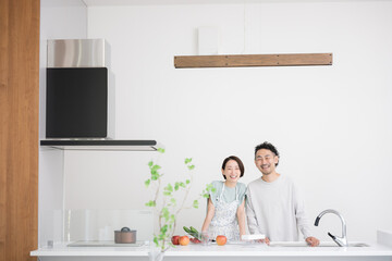 キッチンで笑顔のカメラ目線のミドル夫婦　広角