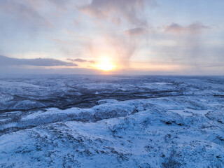 Panoramic aerial view of the vast, rolling, snow-covered forest tundra landscape in the Murmansk region illuminated by a pale, low winter sunset