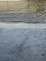Vertical view of floodwater on the road meeting the rough, horizontal edge of light gray concrete pavement after heavy rain.