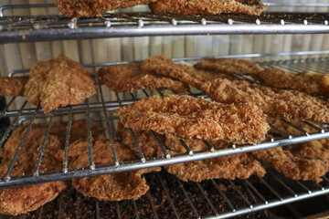 Delicious and appetizing fried chicken breast, crispy golden meat food, resting on metal rack after cooking. This popular and savory meal favorite comfort food dish