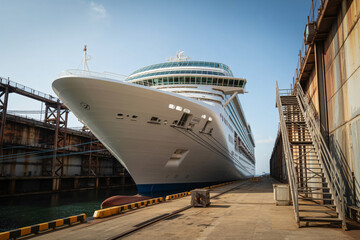 Large cruise ship docked in a dry dock with industrial scaffolding and blue sky overhead
