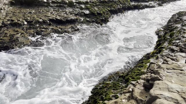 Dynamic tidal action as water floods a shallow crevasse, violently pushing and pulling the ribbons of bright Alaria seaweed back and forth.