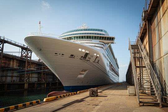 Large cruise ship docked in a dry dock with industrial scaffolding and blue sky overhead