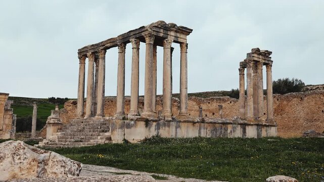 Scenic view of Temple of Juno Caelestis, well-preserved Roman ruins in Dougga, surrounded by spring greenery in Tunisia, against cloudy backdrop