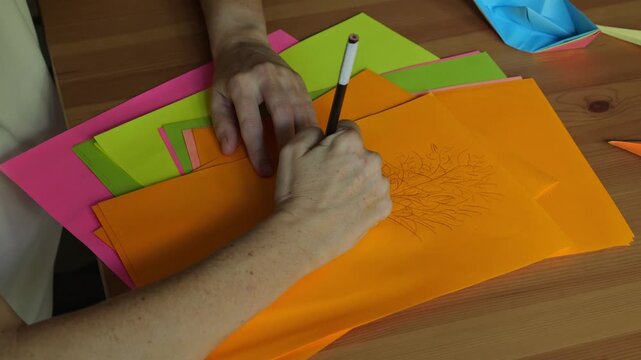 Top view of female hands drawing with pencil on colorful paper sheets