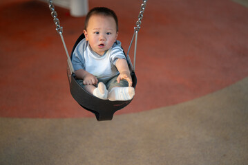 A young Asian boy swings on a swing, gazing at the camera.