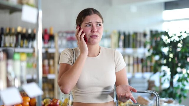 In store, sad girl calls on mobile phone, walks around trading floor and chats, complains to friend, tells sad news. Unhappy girl talking on phone, sharing and telling mother about sorrowful events