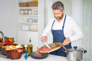 Chef chops vegetables in kitchen. Chef in apron prepares healthy meal with raw ingredients. Cook with vegetables. Chef with fresh vegetables for dinner. Chef prepares breakfast with veggies.