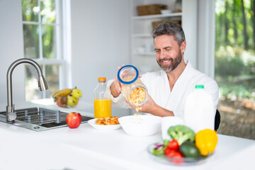 Man eating breakfast in the kitchen on morning. Man enjoys a healthy meal for breakfast. Guy eats cereal and fruit for breakfast in the kitchen. Middle aged man eats vegetables for breakfast.
