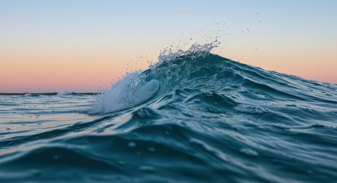 Close up view of a clear blue wave crashing and spraying water in the ocean at sunrise or sunset. Powerful liquid motion and serene nature scene. World Oceans Day.