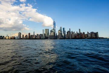 Fototapeta premium New York city. NYC cityscape. Lower Manhattan and One World Trade Center in New York Cit. Skyscrapers of Manhattan located near rippling water of New York bay against blue sky. New York skyscrapers.