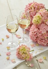 Two glasses of white wine on a white table with purple hydrangea flowers and a pearl necklace for party celebration in the garden of a country house, backyard, patio for banner, poster or card.