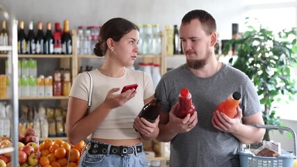 Married couple scans the labels on juice bottles on phone in a supermarket. Wife scans the qr code of the product and shows it to her husband. Visitors to the store buy vegetable and fruit juices - Powered by Adobe