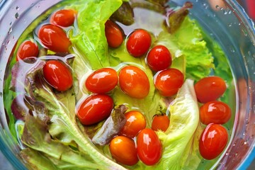 Fresh salad greens and cherry tomatoes soaking in water inside a clear glass bowl