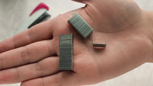 Metal staples in a woman's hand, stapler on a table
