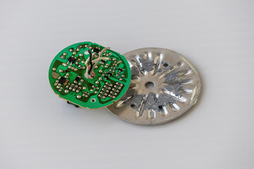Close-up of a disassembled AC/DC Rechargeable LED light bulb circuit board, with electronic components and microchip. Green PCB, technology, engineering, and innovation isolated on white background.