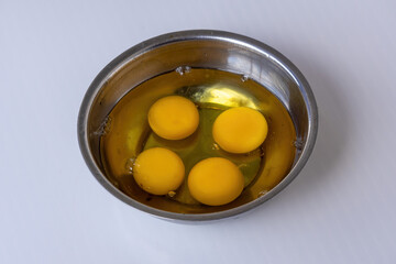 Close-up of four bright yellow egg yolks floating in clear egg white inside a silver steel bowl. Isolated on white background. Perfect ingredients for a healthy omelette or frying.
