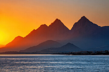 Golden sunrise casting warm light over mountain peaks and calm sea horizon