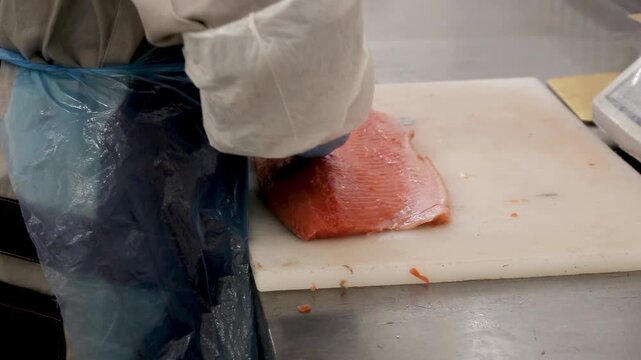 Fish processing worker deboning fish meat with tool on table