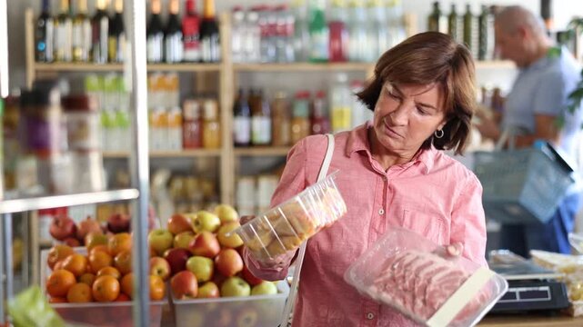 Elderly woman buyer chooses raw chicken and pork in package in grocery store