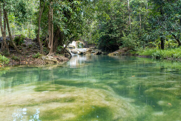 Fototapeta premium A serene tropical waterfall surrounded by lush forest and calm turquoise river water. Ideal for travel, nature, landscape, and eco-tourism themes. 