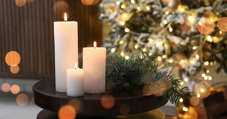 Christmas branches with burning candles on table in living room, closeup