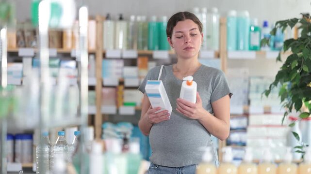 Smiling pregnant woman choosing creams and lotions to moisturize her skin. Woman shopping at pharmacy during pregnancy. High quality 4k footage