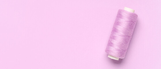 Spool of thread on pink background with space for text, top view