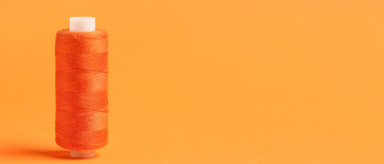 Spool of thread on orange background with space for text