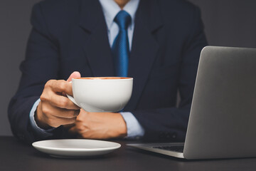 Businessman holding coffee cup while working on laptop.
