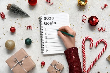 Woman writing down goals for 2025 year in notebook on light background