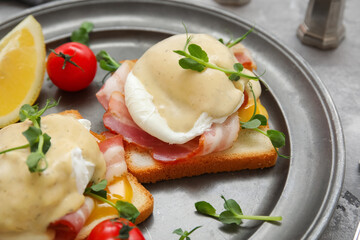 Plate with tasty eggs Benedict, tomatoes and lemon slice, closeup