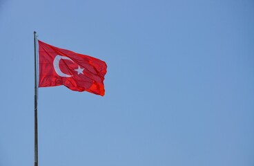 The Turkish flag flutters in the wind against a blue sky
