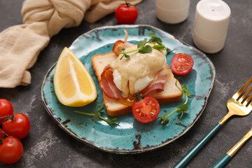 Plate of delicious egg Benedict with bacon and cherry tomatoes on black background, closeup