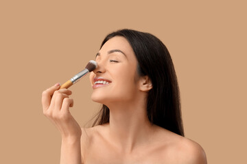 Fototapeta premium Beautiful young woman with makeup brush on brown background
